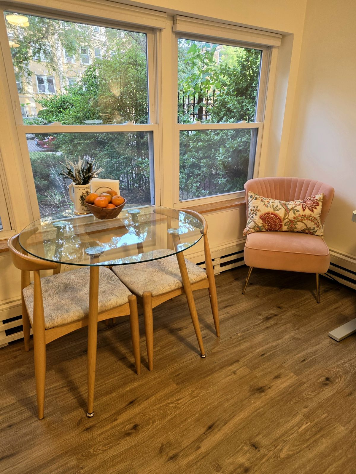 Round glass cafe table with two chairs by the windows, and a blush pink armchair