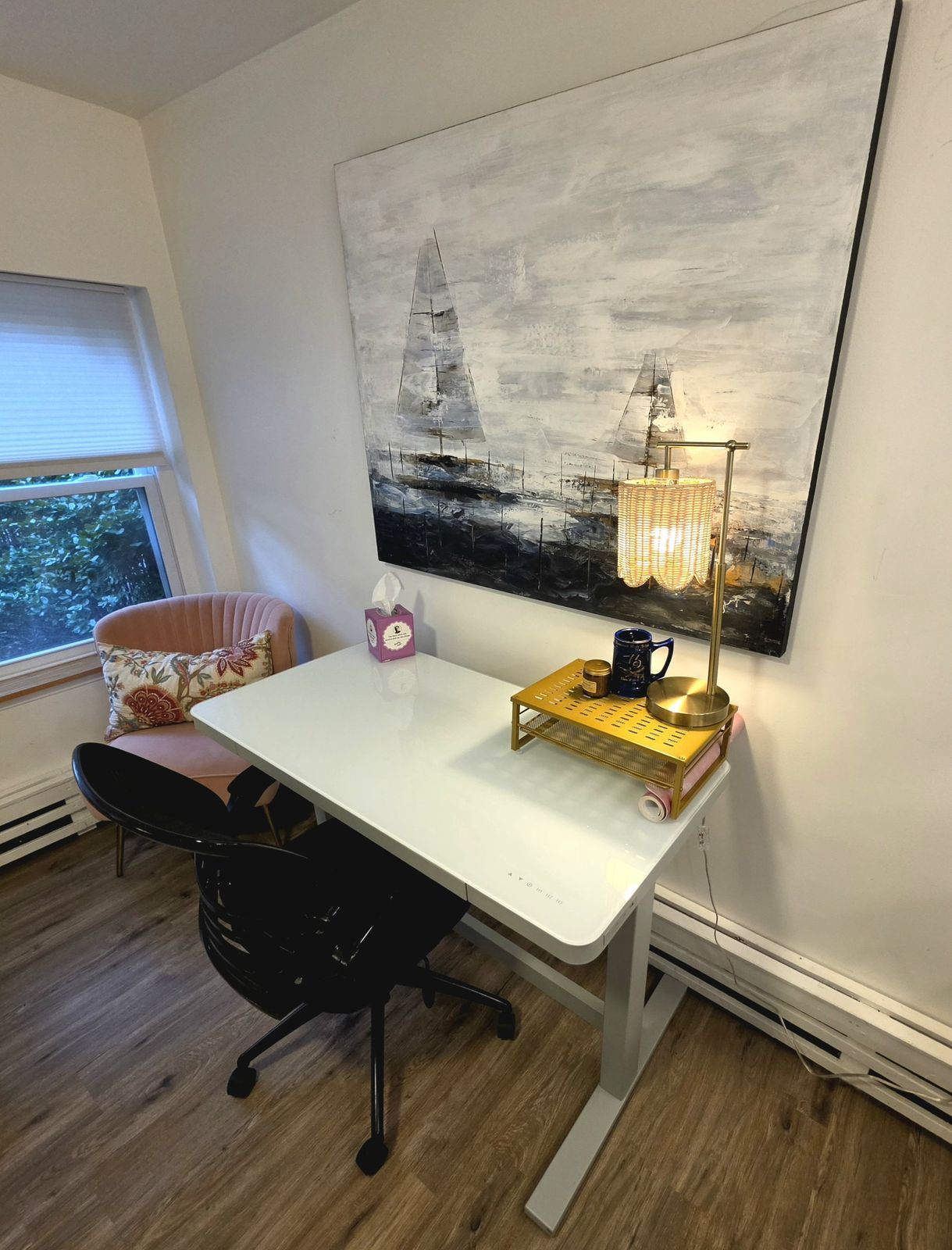 White standing desk with a gold lamp under a large painting of sailboats