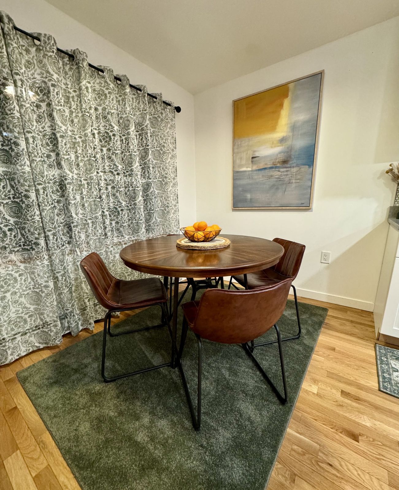 Round dining table with four leather chairs on a green rug