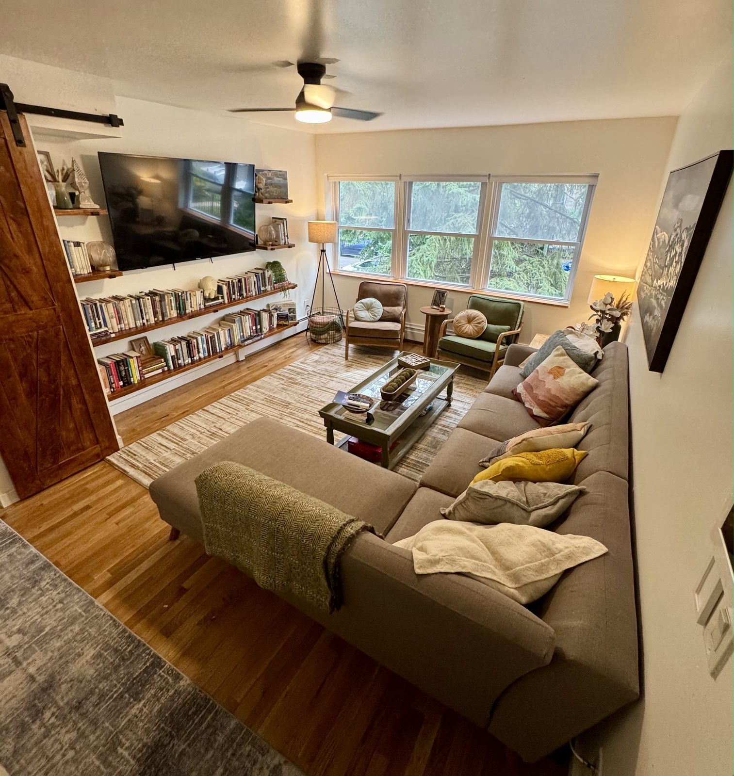 The whole living room: sectional sofa, library wall, television and a row of windows